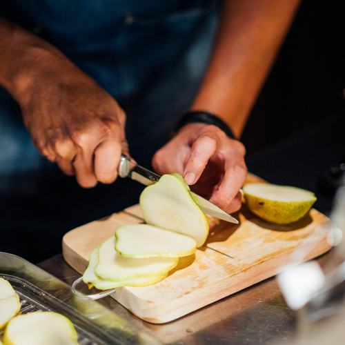 Fruit being sliced thin on a wooden board